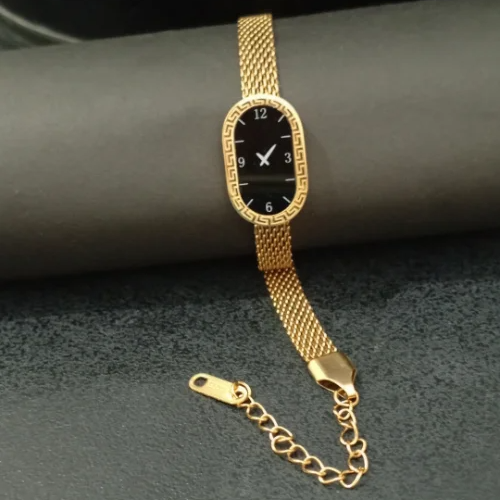 Gold bracelet with a black face watch on a dark surface