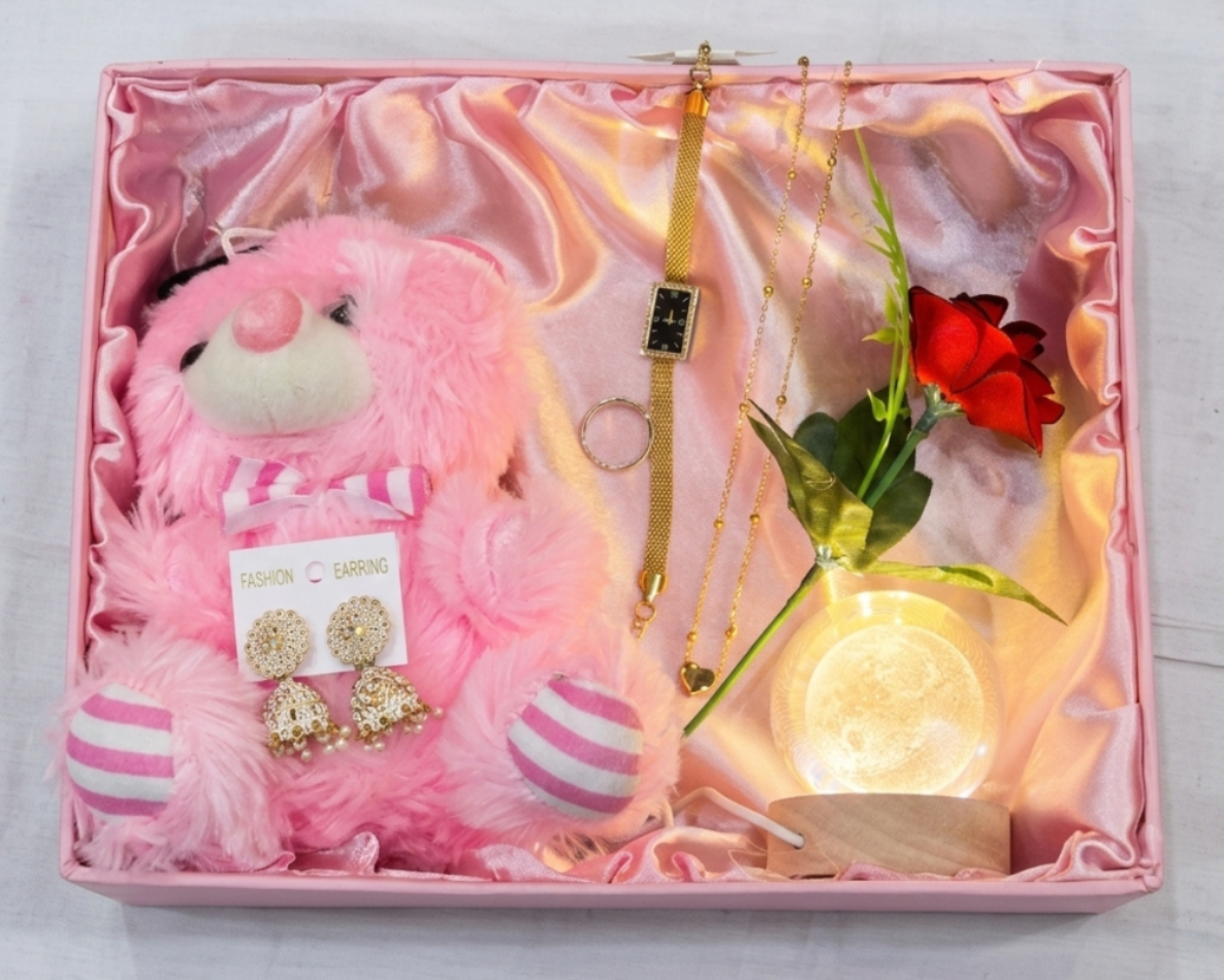 Pink teddy bear, jewelry, and decorative items in a gift box on a white background