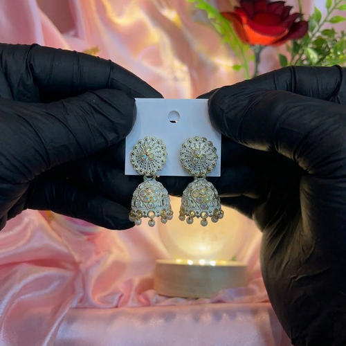 Gold earrings on a card held by hands in black gloves against a soft focus background with flowers.