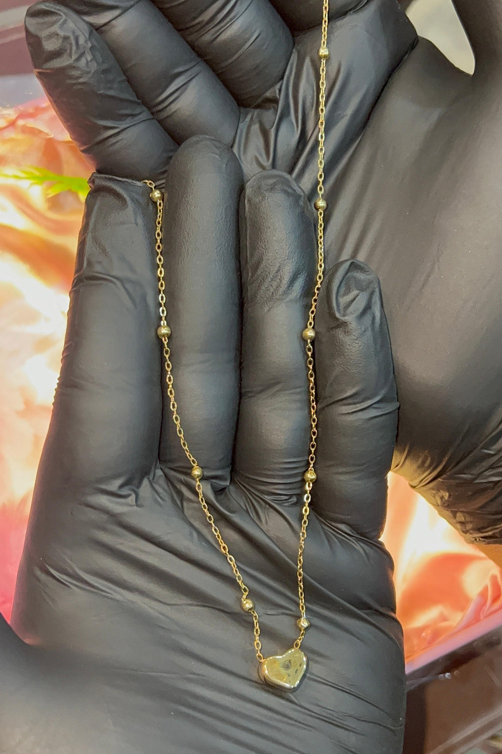 Gold necklace held between fingers with a blurred background