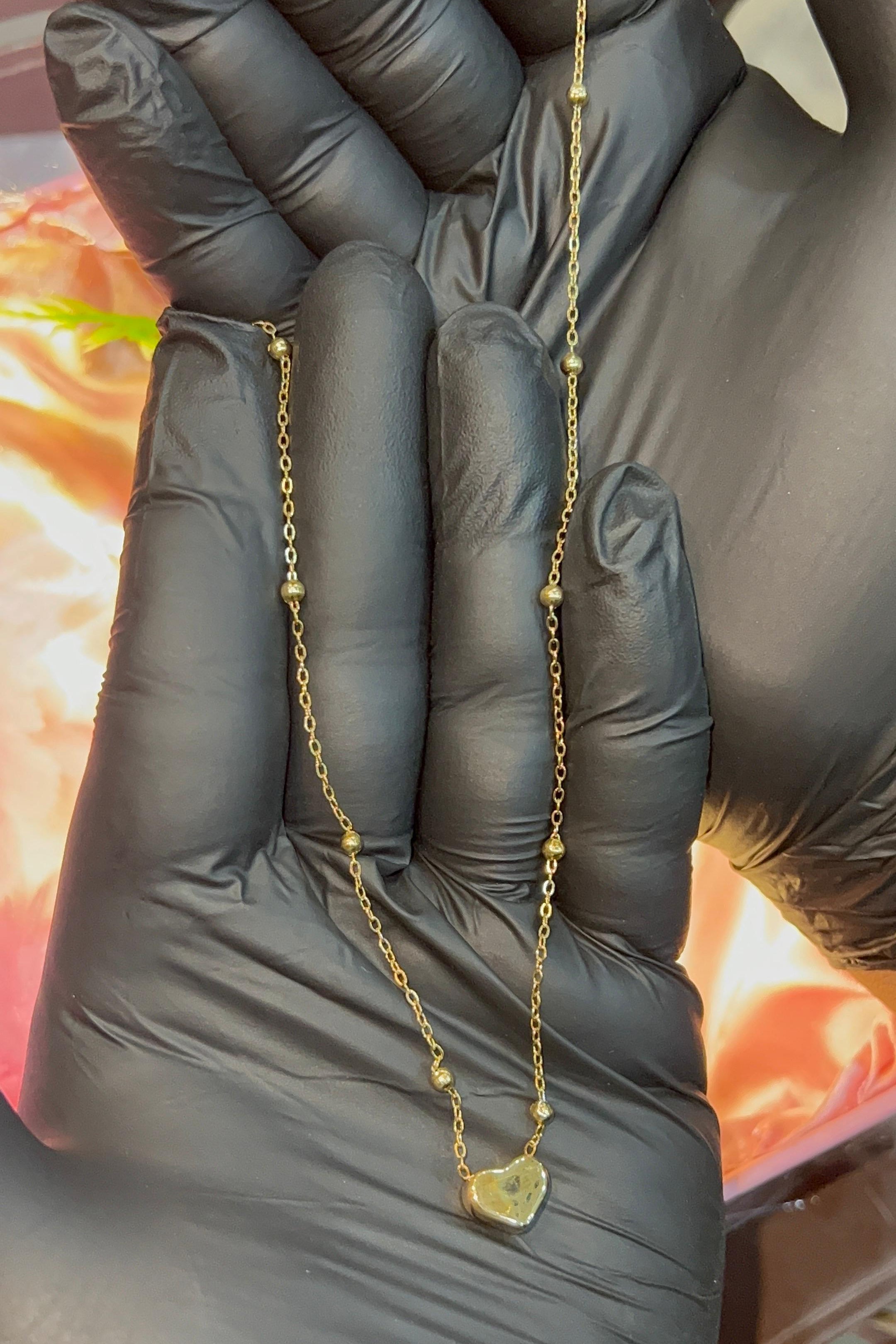 Gold necklace held between fingers with a blurred background