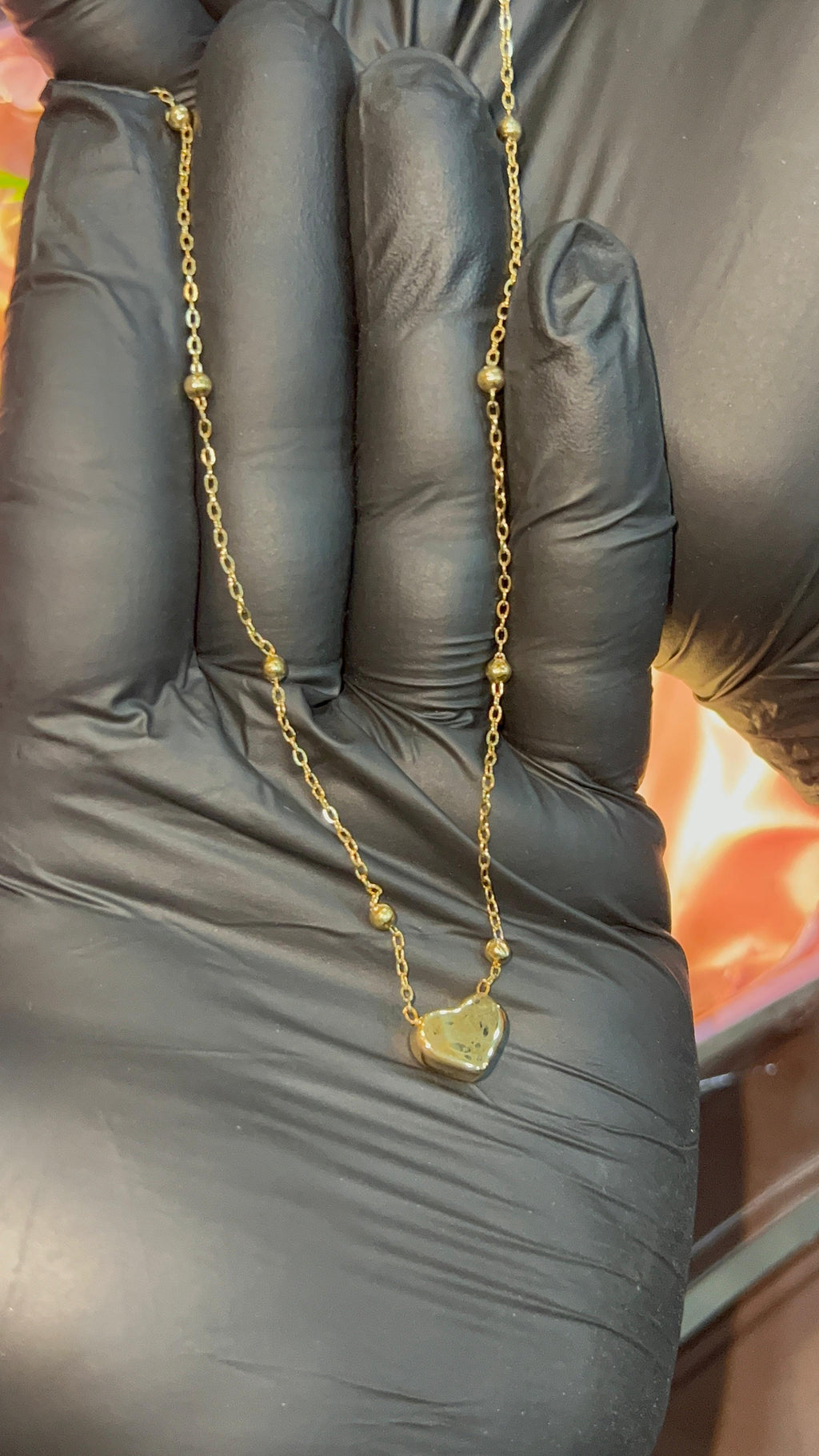 Gold necklace held between black gloved fingers against a blurred background