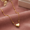 Gold necklace with a heart pendant on a pink fabric background