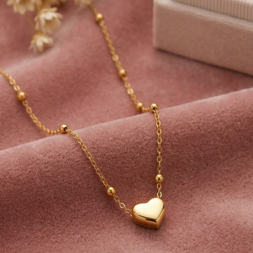Gold necklace with a heart pendant on a pink fabric background
